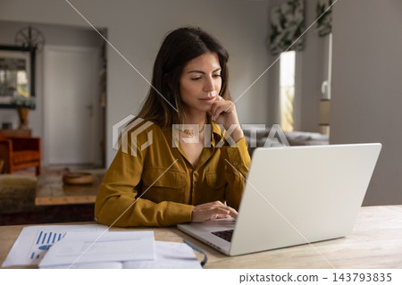 Thoughtful woman reviewing data, examining financial information on laptop Thoughtful woman reviewing data, examining financial information on laptop 143793835