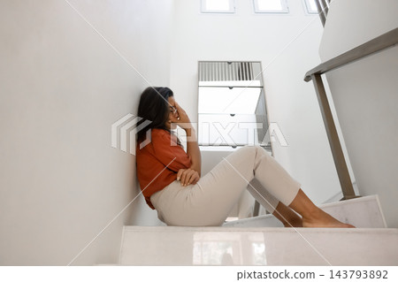 Depressed young woman hunching on stairs hiding face with hand Depressed young woman hunching on stairs hiding face with hand 143793892