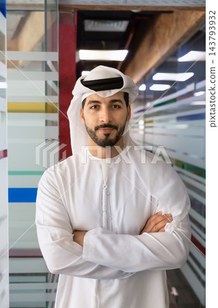 Middle Eastern businessman posing with arms crossed in office corridor 143793932