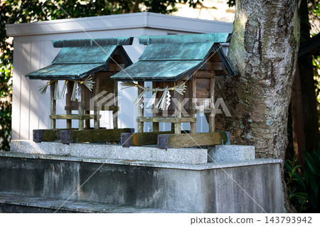 描繪日本宗教祭祀場景,圖中在神社內並排擺放著兩座小型木製神社和神聖的繩索(注連繩),屋頂呈藍綠色,基座為石質。 描繪日本宗教祭祀場景,圖中在神社內並排擺放著兩座小型木製神社和神聖的繩索(注連繩),屋頂呈藍綠色,基座為石質。 143793942