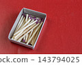 Open matchbox filled with wooden matches lying on a red surface. 143794025