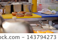 Delicious gourmet burgers stay positioned on yellow work surface during food stall assembly process. Tasty beef cutlets and fresh greens fill open buns beside metal kitchen supplies. 143794273