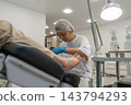 Healthcare worker examines patients foot in clean clinical room, looking closely at toes. Concerned practitioner offers attentive care for discomfort while patient reclines in chair. 143794293