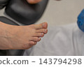 Bare human foot rests comfortably during podiatry examination in clinical medical office. Professional healthcare setting provides calm environment for routine foot care checkup. 143794298
