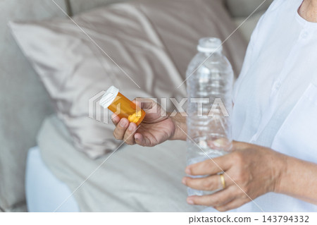 Senior woman taking medication with water at home for health management. Senior woman taking medication with water at home for health management. 143794332