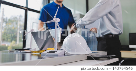 Two Asian engineers wearing hardhats and safety vests discussing solar panel installation and renewable energy project in the office. Two Asian engineers wearing hardhats and safety vests discussing solar panel installation and renewable energy project in the office. 143794546