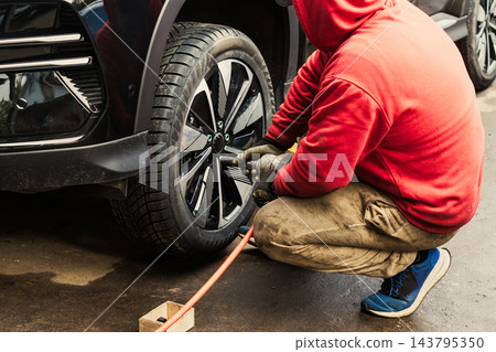 Worker changes tire on black SUV in auto repair shop during daytime hours Worker changes tire on black SUV in auto repair shop during daytime hours 143795350