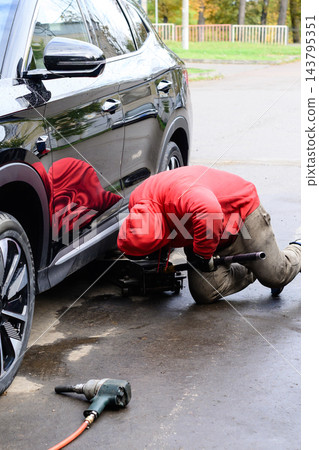 Man works on car at garage in autumn season while using tools to repair vehicle tires and components for maintenance and safety checks Man works on car at garage in autumn season while using tools to repair vehicle tires and components for maintenance and safety checks 143795351