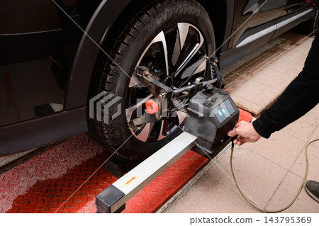Wheel alignment and alignment on the car service platform. Vehicle wheel alignment taking place in auto repair shop during daytime hours Wheel alignment and alignment on the car service platform. Vehicle wheel alignment taking place in auto repair shop during daytime hours 143795369