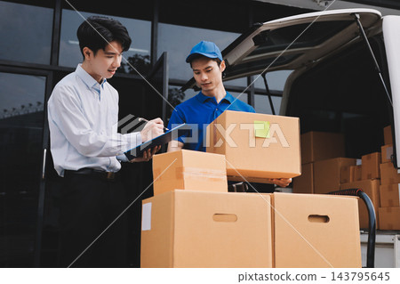 Young businessman signing a delivery receipt document on a clipboard held by a courier in a blue uniform. Young businessman signing a delivery receipt document on a clipboard held by a courier in a blue uniform. 143795645