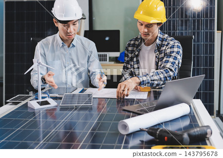 Two Asian engineers wearing hardhats and safety vests discussing solar panel installation and renewable energy project in the office. Two Asian engineers wearing hardhats and safety vests discussing solar panel installation and renewable energy project in the office. 143795678