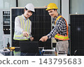 Two Asian engineers wearing hardhats and safety vests discussing solar panel installation and renewable energy project in the office. 143795683