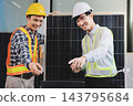 Two Asian engineers wearing hardhats and safety vests discussing solar panel installation and renewable energy project in the office. 143795684