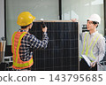 Two Asian engineers wearing hardhats and safety vests discussing solar panel installation and renewable energy project in the office. 143795685