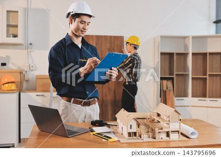 Asian architect and engineer team checking architectural house model using measuring tape on the table at office studio. Asian architect and engineer team checking architectural house model using measuring tape on the table at office studio. 143795696