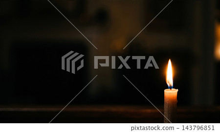 Single burning candle flame illuminating dark room interior for funeral vigil memorial service condolence death loss remembrance mourning and grief prayers 143796851
