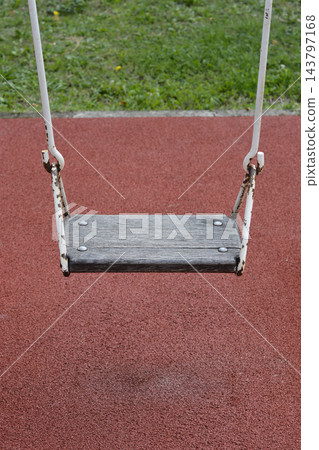An empty wooden swing at a playground with a red rubber surface An empty wooden swing at a playground with a red rubber surface 143797168