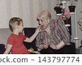 An elderly woman a grandmother brings fruit on a plate to her young grandson in the room and feeds him. Caring for children and the elderly parental love. 143797774
