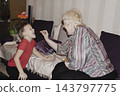 An elderly woman a grandmother brings fruit on a plate to her young grandson in the room and feeds him. Caring for children and the elderly parental love. 143797775