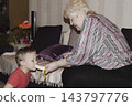 An elderly woman a grandmother brings fruit on a plate to her young grandson in the room and feeds him. Caring for children and the elderly parental love. 143797776