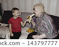 An elderly woman a grandmother brings fruit on a plate to her young grandson in the room and feeds him. Caring for children and the elderly parental love. 143797777