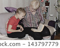 grandmother is reading colorful book grandson, has leaned in closer to listen. grandmother wearing glasses, boy, dressed red T-shirt, is intently examining the book and listening to the story. 143797779