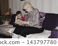 grandmother is reading colorful book grandson, has leaned in closer to listen. grandmother wearing glasses, boy, dressed red T-shirt, is intently examining the book and listening to the story. 143797780