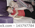 grandmother is reading colorful book grandson, has leaned in closer to listen. grandmother wearing glasses, boy, dressed red T-shirt, is intently examining the book and listening to the story. 143797784