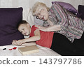 grandmother is reading colorful book grandson, has leaned in closer to listen. grandmother wearing glasses, boy, dressed red T-shirt, is intently examining the book and listening to the story. 143797786