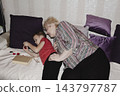 grandmother is reading colorful book grandson, has leaned in closer to listen. grandmother wearing glasses, boy, dressed red T-shirt, is intently examining the book and listening to the story. 143797787