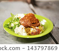 Indonesian crispy fried duck or bebek goreng served over steamed rice with serundeng, sambal green chili, and fresh basil leaves on green plate 143797869