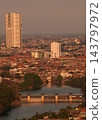 High angle view of urban cityscape with river water dam, tall skyscraper building, and dense residential houses during sunset 143797972