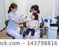 A 2-year-old girl and her mother receiving toothbrushing instruction at a dental clinic. 143798816