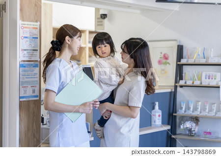 一位微笑的牙科保健員和她的母親抱著一個兩歲的小女孩。 143798869