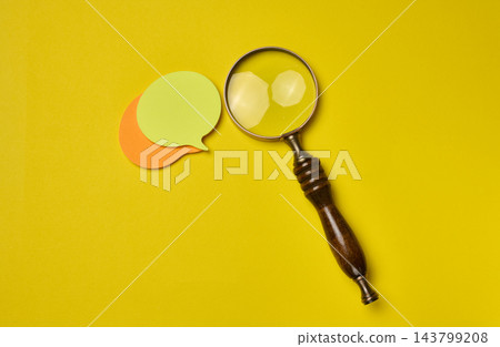 Magnifying glass with a wooden handle and multicolor speech bubbles on a yellow background. Magnifying glass with a wooden handle and multicolor speech bubbles on a yellow background. 143799208