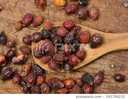 Dried rosehip fruits in a wooden spoon and on a table close-up. Dried rosehip fruits in a wooden spoon and on a table close-up. 143799232