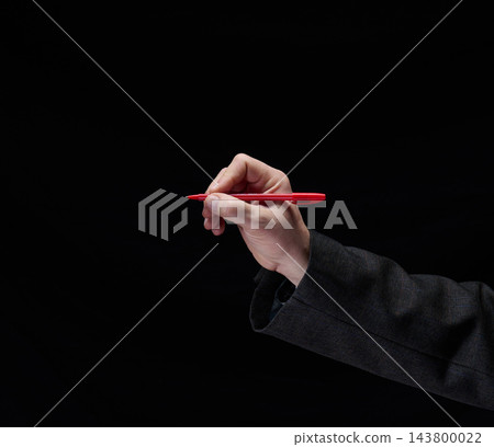Man's hand in a suit jacket holding a red pen ready to write or sign a document on a dark background Man's hand in a suit jacket holding a red pen ready to write or sign a document on a dark background 143800022
