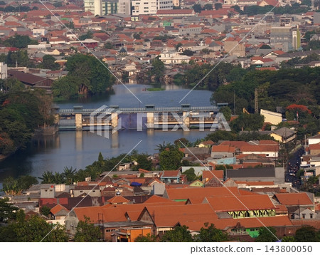 Aerial high angle view of river water dam and watergate surrounded by dense residential houses and cityscape in Surabaya Aerial high angle view of river water dam and watergate surrounded by dense residential houses and cityscape in Surabaya 143800050