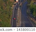 Top down aerial view of curved asphalt road with median divider and cars driving through green trees along highway 143800110