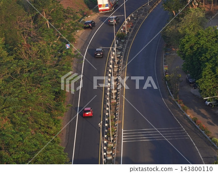 Top down aerial view of curved asphalt road with median divider and cars driving through green trees along highway Top down aerial view of curved asphalt road with median divider and cars driving through green trees along highway 143800110