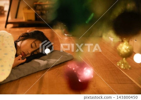 一個孩子睡在聖誕樹旁的毯子下。 一個孩子睡在聖誕樹旁的毯子下。 143800450