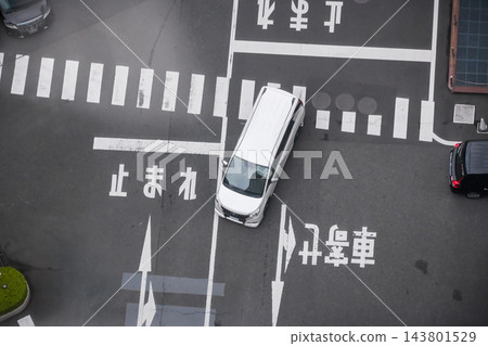 從上方俯瞰一輛白色小型貨車斜穿過十字路口,路口設有行人過街標誌和停車線。 從上方俯瞰一輛白色小型貨車斜穿過十字路口,路口設有行人過街標誌和停車線。 143801529