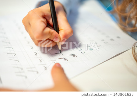 First grade student practices writing letters with pencil in workbook. Early literacy and handwriting skills develop with selective focus and shallow depth of field First grade student practices writing letters with pencil in workbook. Early literacy and handwriting skills develop with selective focus and shallow depth of field 143801623