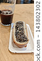An open faced sandwich with a dark textured topping rests on a paper plate beside a partially filled glass of dark beer on wood 143802302