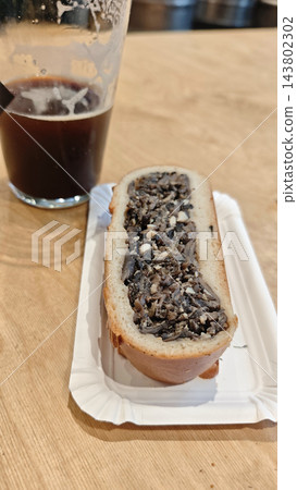An open faced sandwich with a dark textured topping rests on a paper plate beside a partially filled glass of dark beer on wood An open faced sandwich with a dark textured topping rests on a paper plate beside a partially filled glass of dark beer on wood 143802302