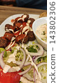 Meatballs with creamy sauce, salad, tomato, and dip arranged on a white plate over a wooden table, close up of a plated meal 143802306