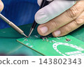 Close-up of a skilled operator wearing rubber finger cots soldering an electronic PCB board 143802343