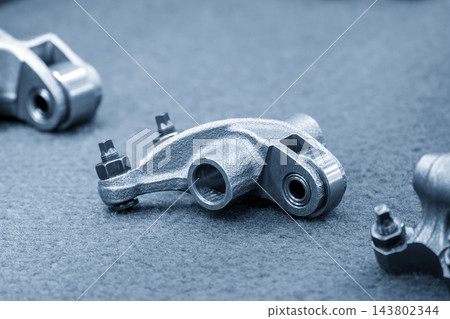 Close-up of automotive roller rocker arm parts in a modern blue tone scene Close-up of automotive roller rocker arm parts in a modern blue tone scene 143802344