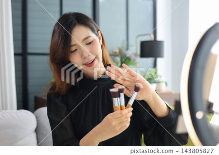Female content creator filming beauty vlog holding cosmetics brushes for social media video production. Female content creator filming beauty vlog holding cosmetics brushes for social media video production. 143805827