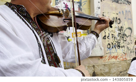 Adult man wearing a traditional embroidered vyshyvanka plays a vintage violin on city street. The scene emphasizes cultural identity, heritage and the expressive character of live music. Slow mo Adult man wearing a traditional embroidered vyshyvanka plays a vintage violin on city street. The scene emphasizes cultural identity, heritage and the expressive character of live music. Slow mo 143805859
